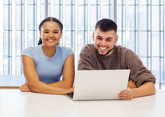 A male student and female student sitting at table inside with an open laptop