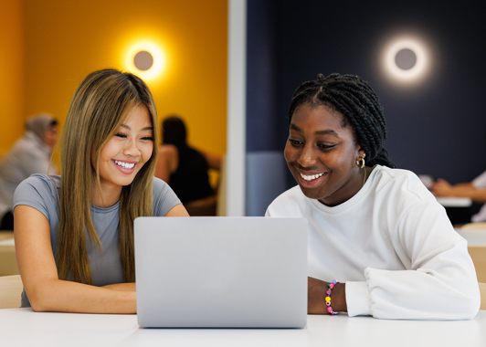 Two female students sitting at table inside with an open laptop researching how to get to university with no ATAR